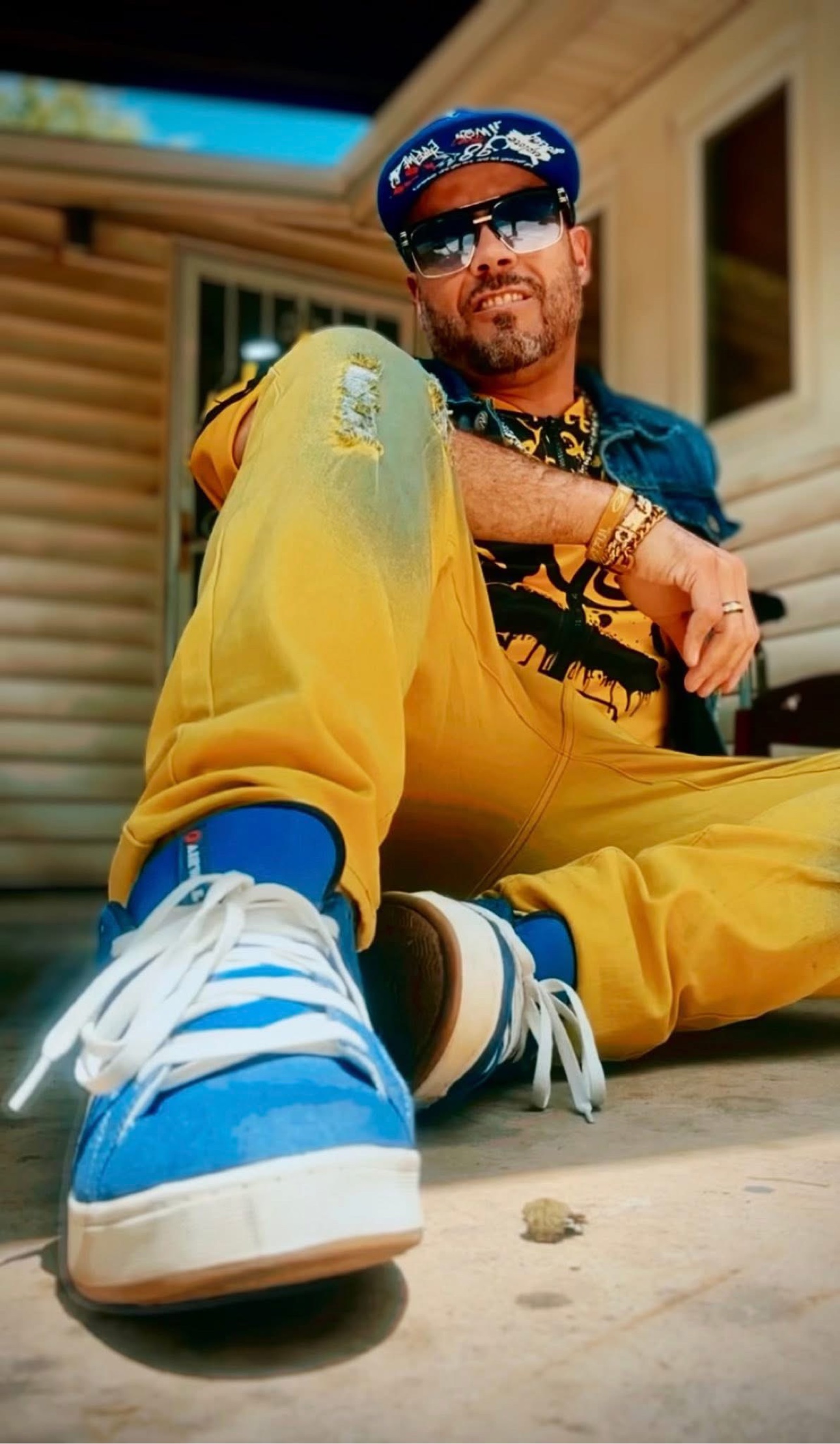 Patrick Quezada sitting outdoors in a yellow outfit, blue cap and sunglasses